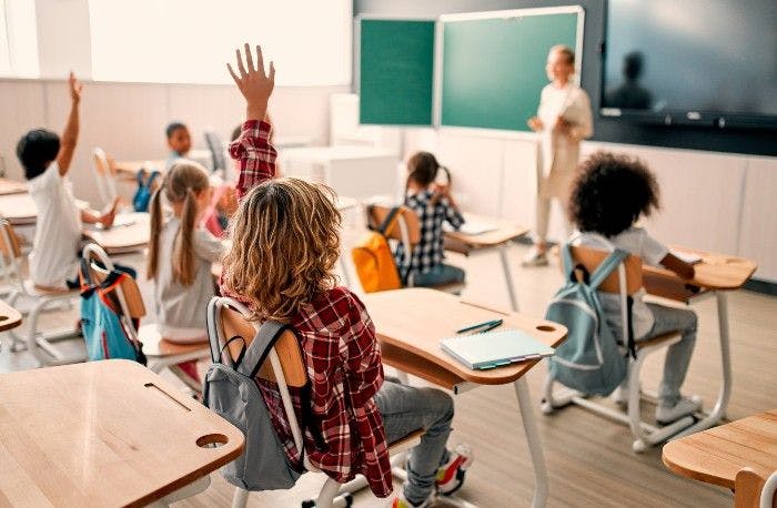 kids sitting in classroom with hands raised